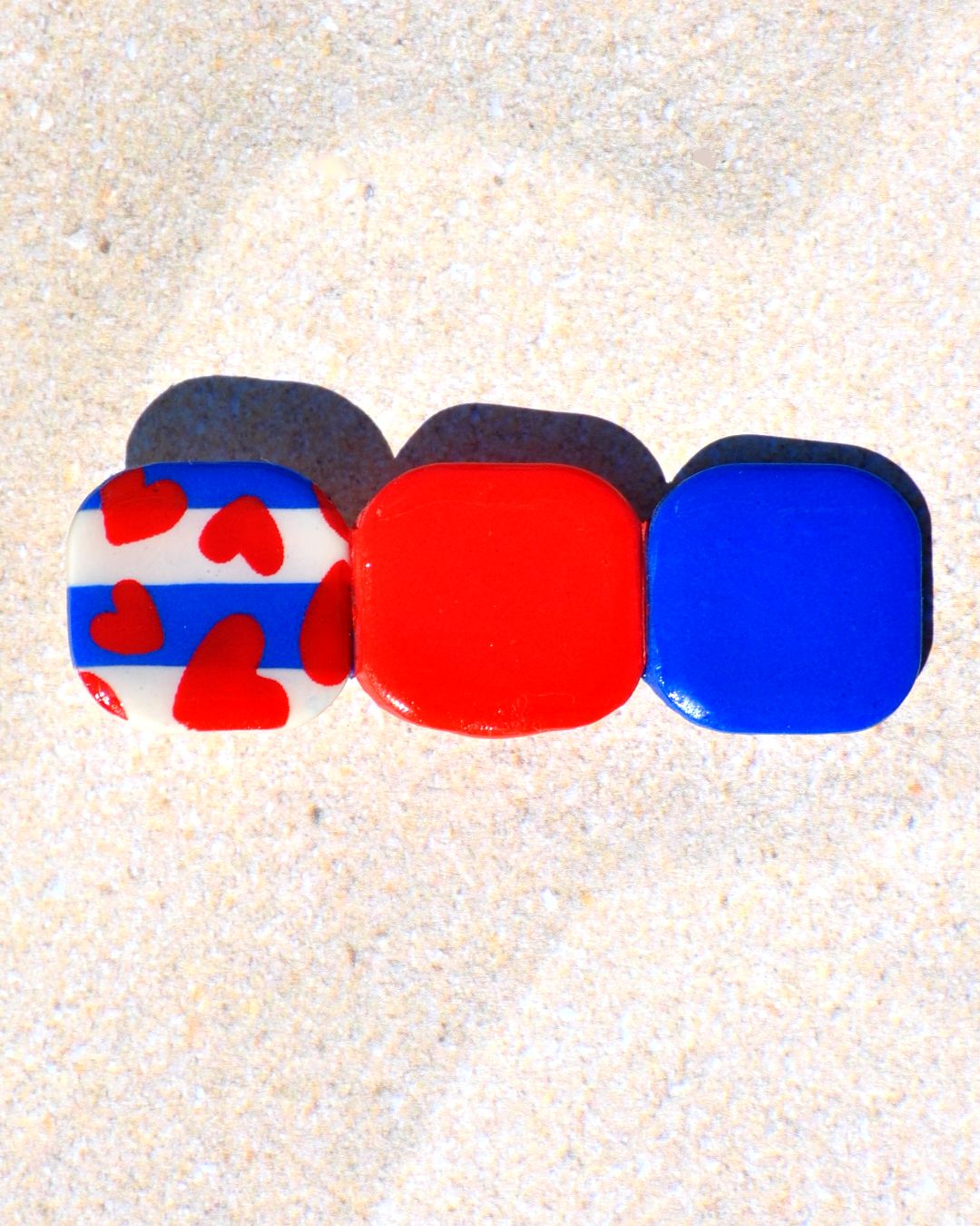 Barrette composée de trois carrés retro, un motif marinière avec cœurs rouges, un rouge vif et un bleu éclatant.