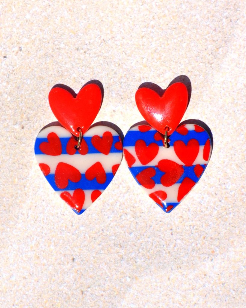 Paire de boucles d'oreilles deux cœurs superposés: la puce est un petit cœur rouge qui surmonte un autre cœur au motif marinière avec des cœurs rouges.