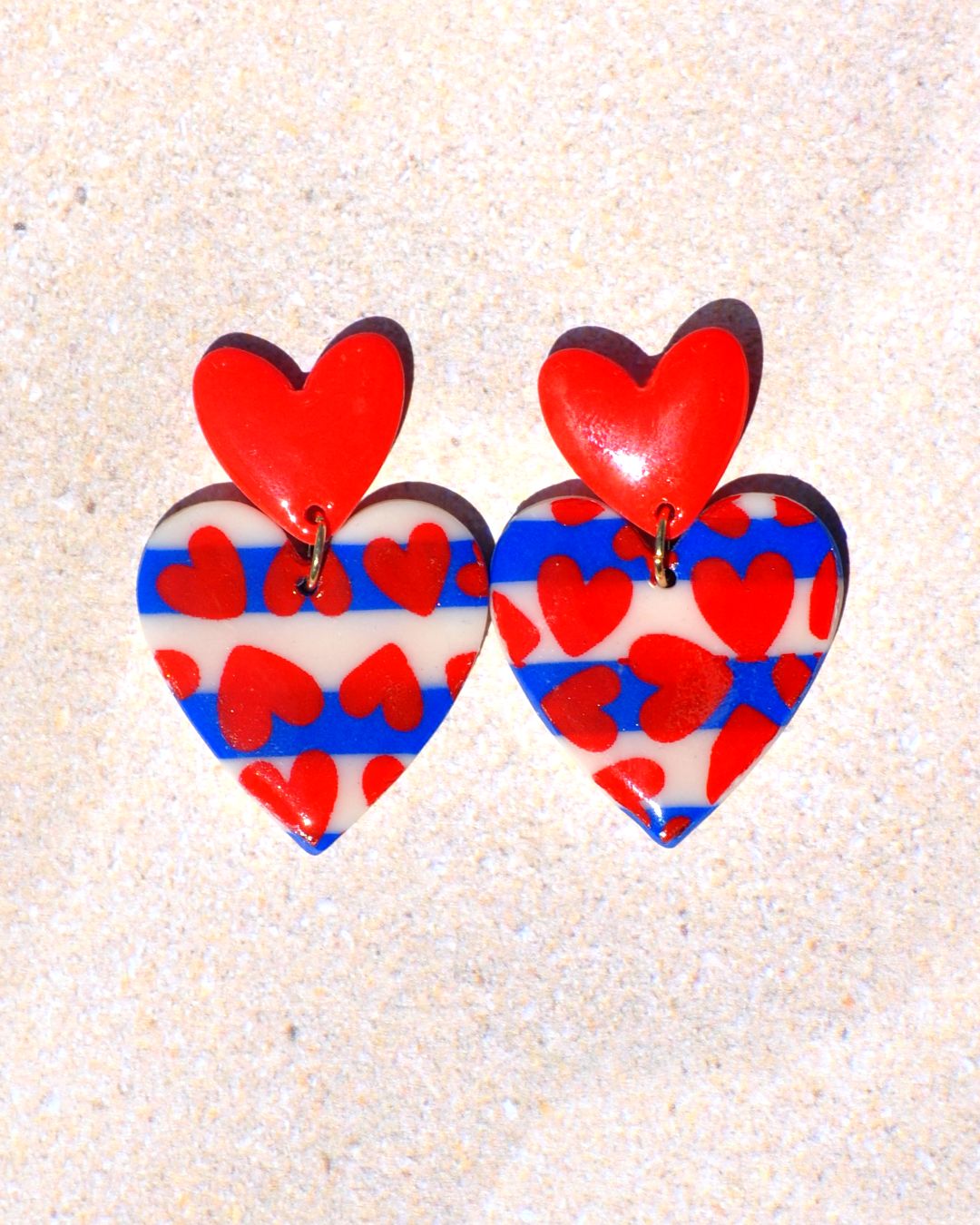 Paire de boucles d'oreilles deux cœurs superposés: la puce est un petit cœur rouge qui surmonte un autre cœur au motif marinière avec des cœurs rouges.