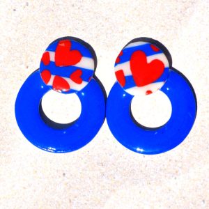 Paire de boucles d'oreilles en forme de cercle ajouré. Une grosse puce ronde en relief est collée sur le haut de la boucle. La boucle est unie bleu éclatant. La "puce" ronde est au motif marinière cœurs rouges.