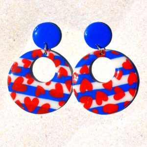 Paire de boucles d'oreilles en forme de rond rétro, ajourée, au motif marinière et cœurs rouges, surmontée d'une puce ronde unie bleue éclatante.