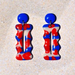 Paire de boucles d'oreilles en forme "petit lu" festonné allongé. La paire de boucles d'oreilles est ajourée au centre d'une ellipse très fine. Une petite puce unie bleu éclatant surmonte une boucle motif marinière cœurs rouges.