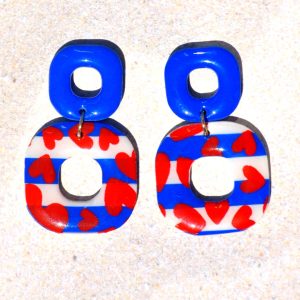 Paire de boucles d'oreilles duo de carrés aux bords arrondis. Un petit carré bleu éclatant surmonte un plus gros carré marinière à cœurs rouges.