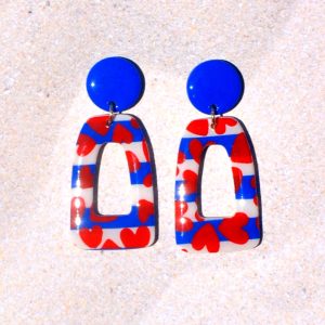 Paire de boucles d'oreilles en deux parties. Une puce ronde unie bleue éclatante surmonte un quadrilatère trapézoïde ajouré, au motif marinière cœurs rouges.